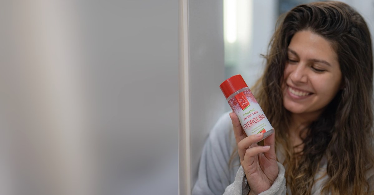 Žena s vodicom za usta od rujevine Hydrolina pred ogledalom, njega kod afti na jeziku